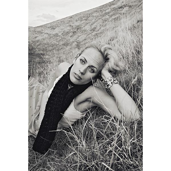 Model lies on hill. She leans toward the camera with her head on her hand.